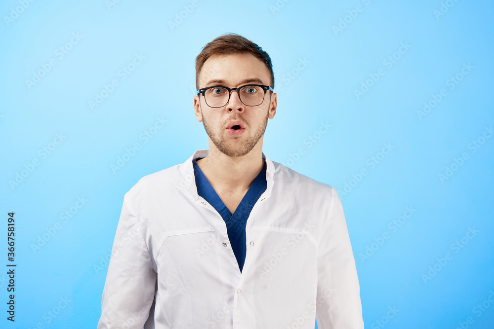 Shocked doctor in white coat opened his mouth in surprise isolated on blue background Shocked doctor in white coat opened his mouth in surprise isolated on blue background