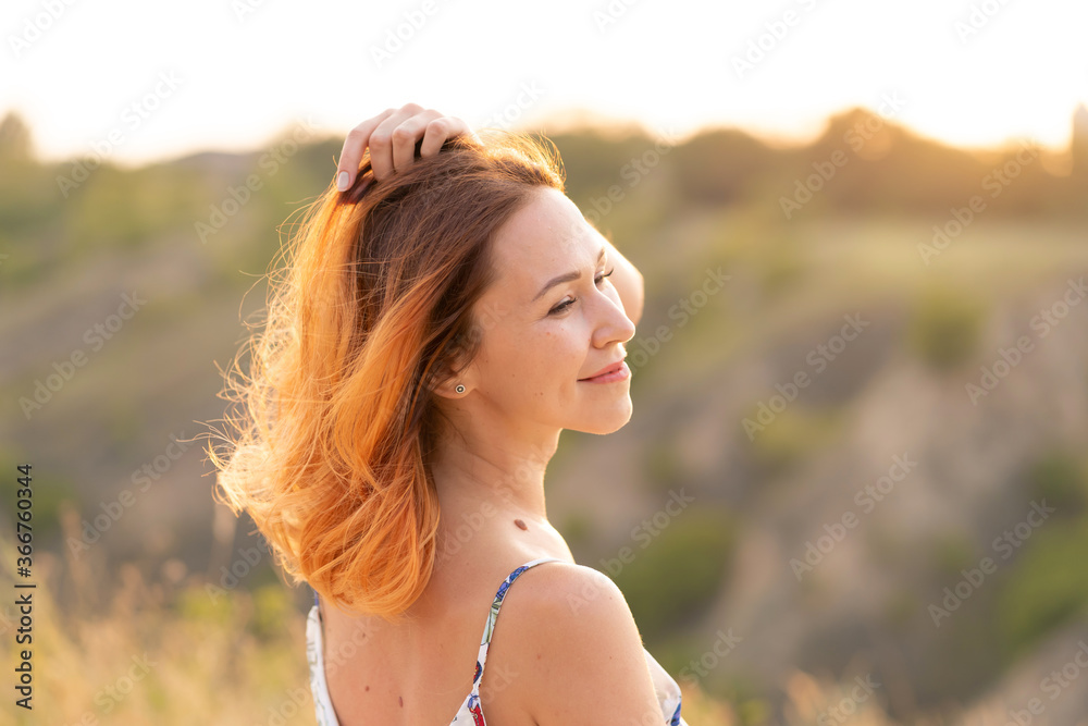 Tender beautiful red-haired girl enjoys the sunset in a field with a hill. Tender beautiful red-haired girl enjoys the sunset in a field with a hill.