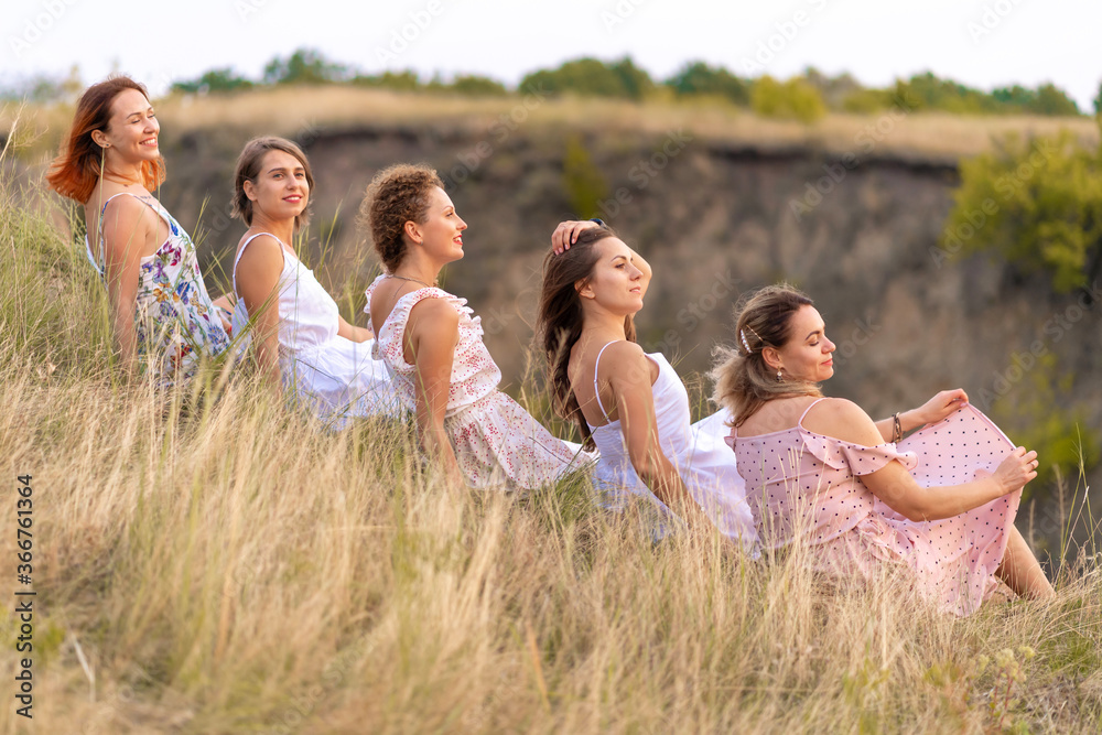 Naklejka premium A cheerful company of beautiful girls friends enjoy a picturesque panorama of the green hills at sunset