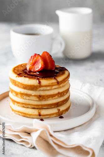 Stack of classic american pancakes with strawberry and sirop . black coffee cup and milk on the white table. Copy space