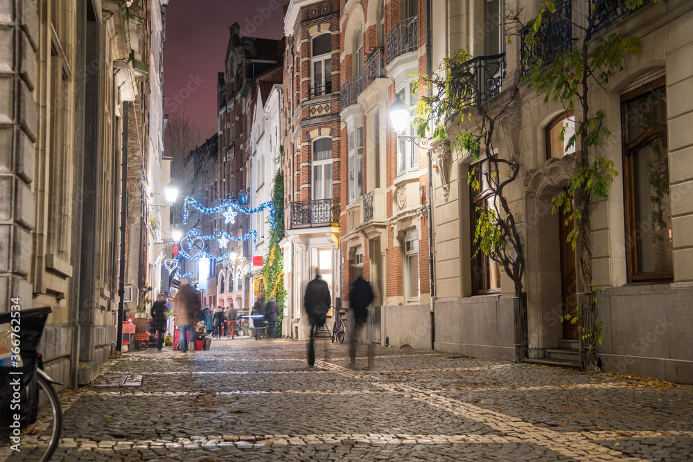 Cobblestone pedestrian street lined with historic buildings in a old city centre at night in winter. Antwerp, Belgium.