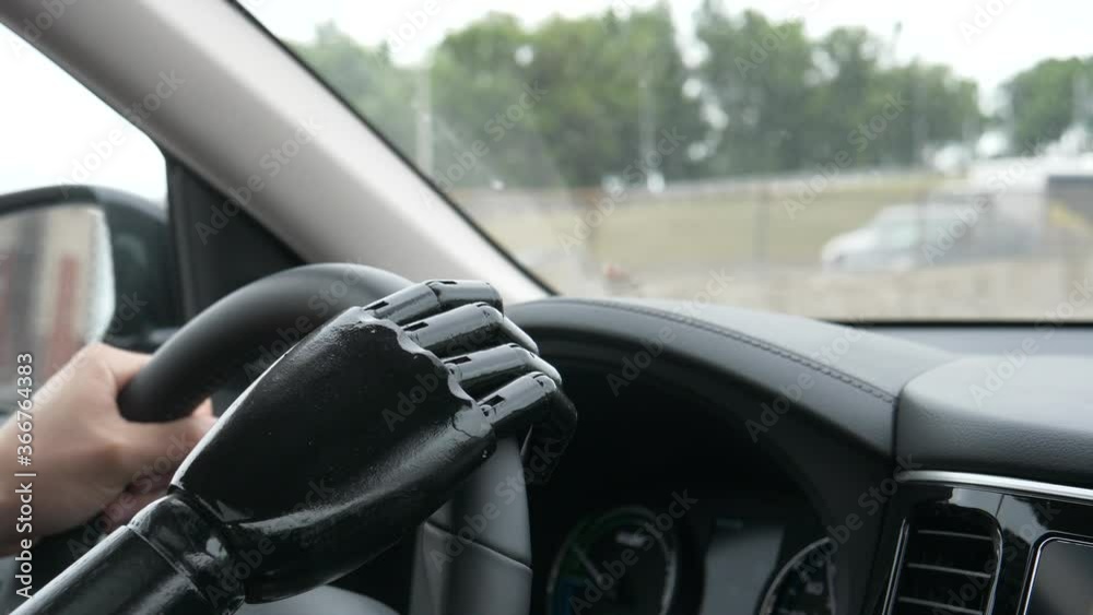 A young man driving his car with his fake hand holding the steering wheel. Handicap person living with an artificial limb. Closeup shot. A young man driving his car with his fake hand holding the steering wheel. Handicap person living with an artificial limb. Closeup shot.