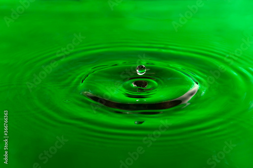Drop green color falling and forming waves ripples
