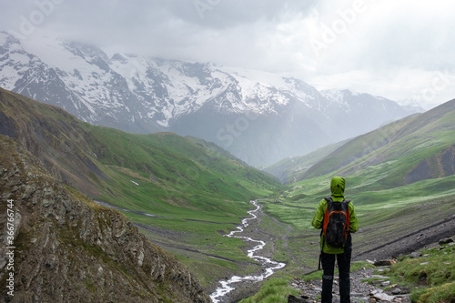 Trekking person in path with clouds, rain and bad weather covered in rain protective equipment in alpine mountain pass of the alps
