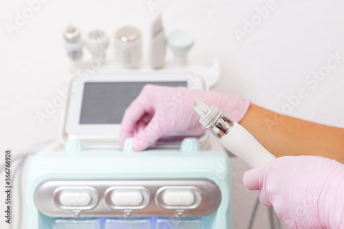 Beauty salon. The cosmetologist holds the device for the water peeling procedure in his hands and turns on the device. Professional skin care and beauty concept