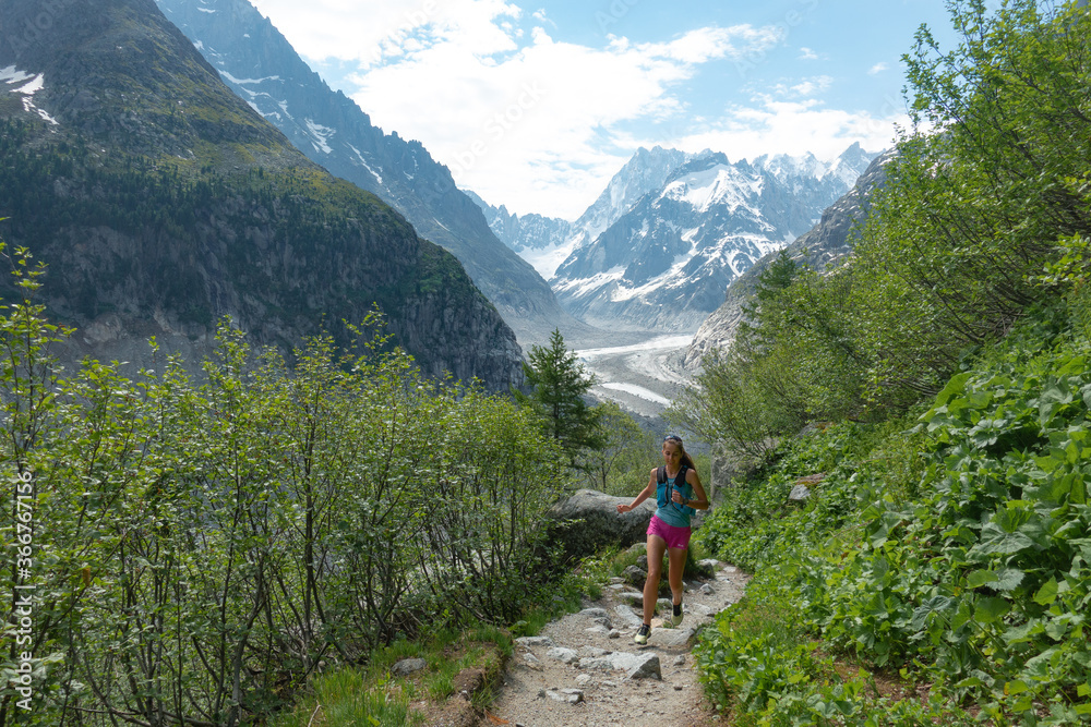Trail runner woman running with scenic view Mer du Glace Glacier in Mont Blanc Mountain Ridge in Chamonix, France
