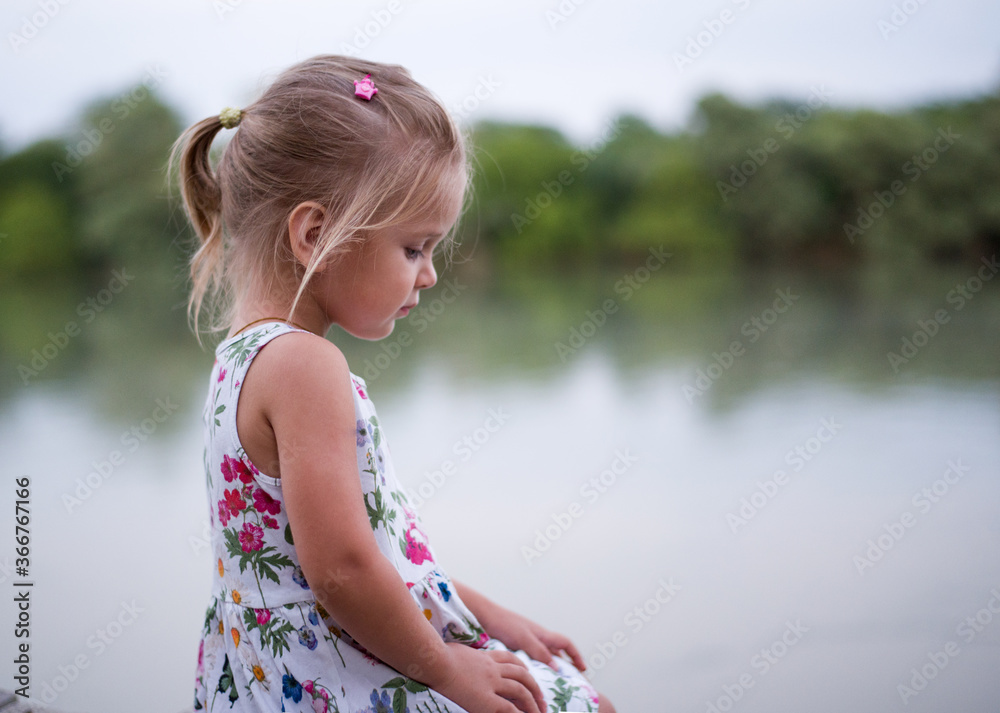 little girl on the river. Little sad girl sits on the pier by the river ...