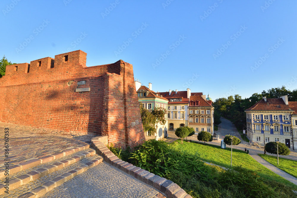 The historic defensive walls of the Warsaw Barbican and burgher houses in the Old Town in the light of the rising sun.