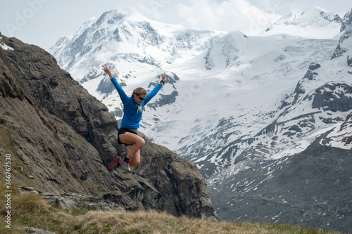 Trail runner woman jumping happily in alpine mountains with snow and glacier in the background