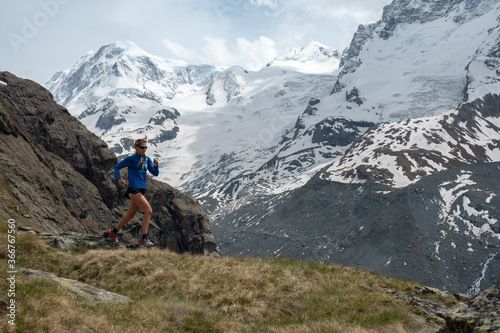 Fotografie, Obraz Woman trail runner in alpine mountains with snow and glacier in the background