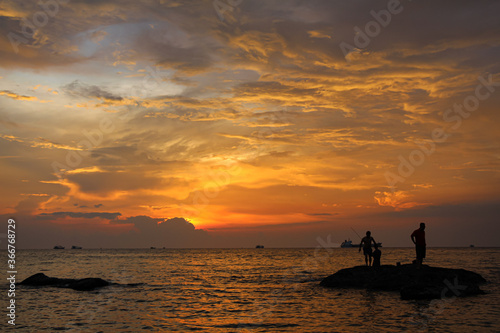 A silhouette of fishermen standing on rocks at sunset at Ba Keo Beach