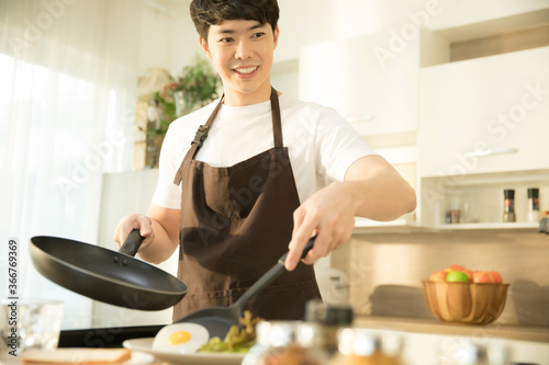 Young man is  cooking  sunny side up egg and salad for breakfast