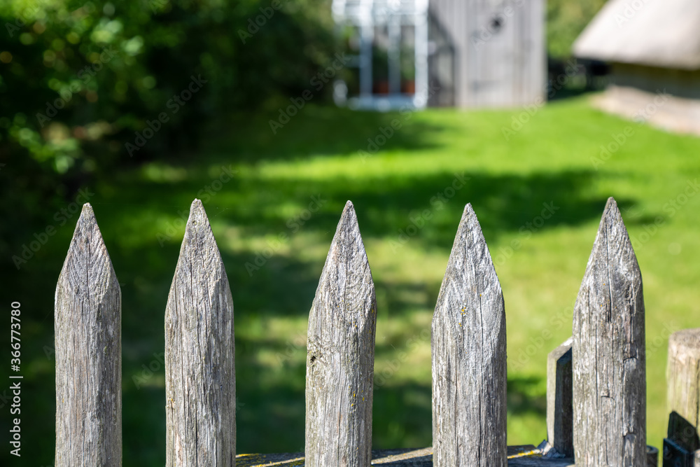 Ein Holzzaun mit Spitzen  vor einem Garten