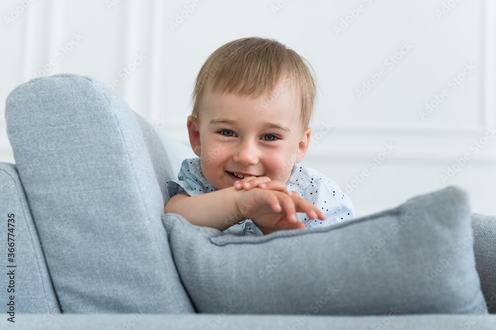 portrait of a little smiling boy child playing on the sofa in living room