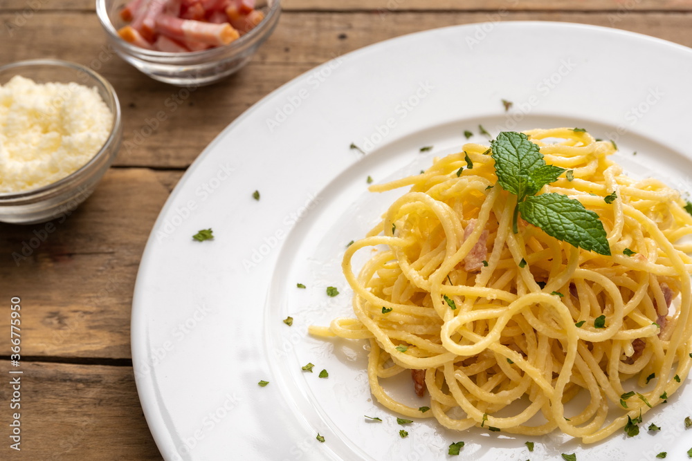 Spaghetti a la carbonara on a white plate and rustic table