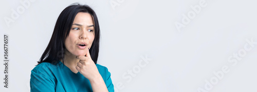 Portrait of a beautiful girl  in a blue t-shirt, looks aside with pensive expression, is considering a plan for further action.