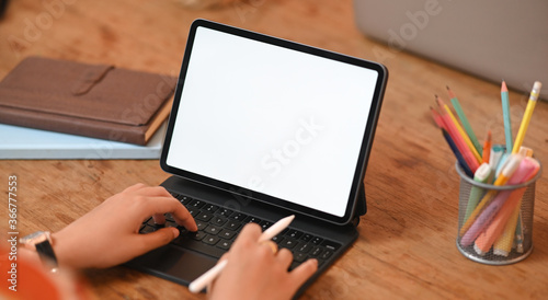 Cropped image hands are using a computer tablet at the wooden working table.