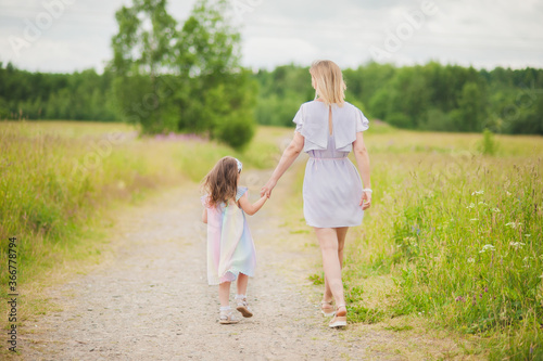 Mother and daughter hold hands on the road in the Park. Mother and daughter walk hand in hand on the road to the field in the summer.