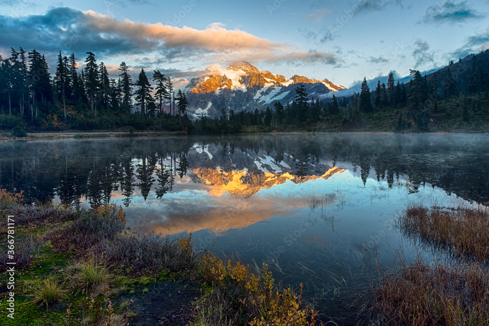 Misty sunset at Mirror Lake in the North Cascades National park in Washington, USA. Mt. Shukson reflects last rays of sun. Light fog over water