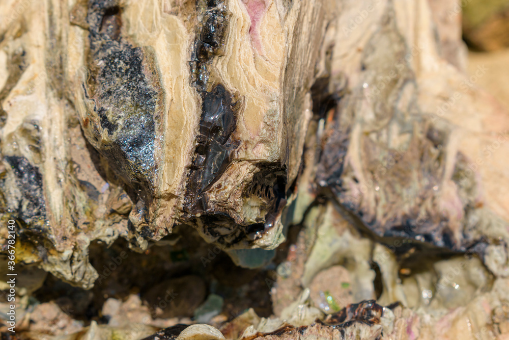 Fused rocks. Lamellar stone texture. Burnt black surfaces. Multi-colored shine of minerals. Selective focus.
