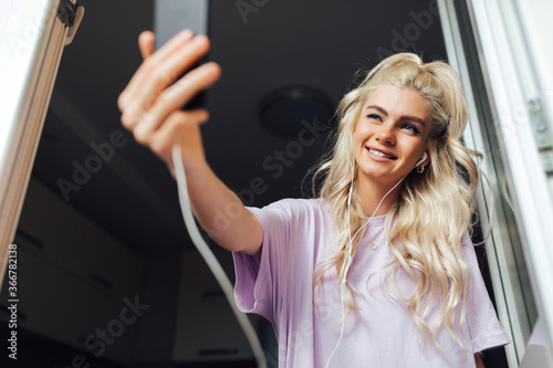 Happy blonde woman making facetime video calling with smartphone at home, using zoom meeting online app, social distancing, work from home, work remotely concept. Gadget addiction. Making selfie.