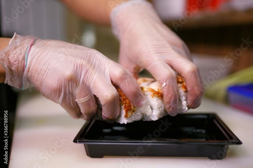 close up of gloved hands putting sushi in a box