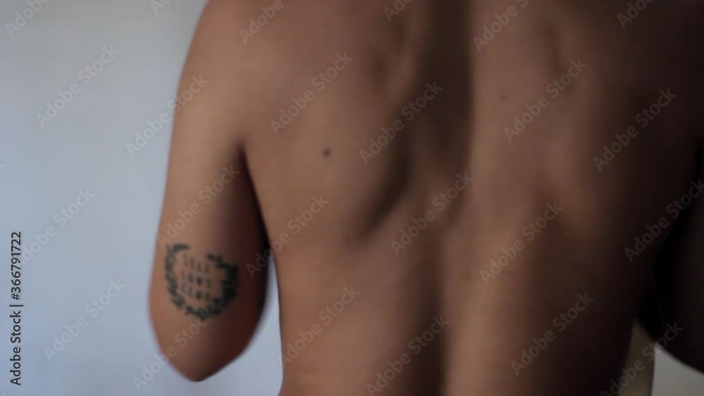 Bare back of a woman on a white background, putting on a beige nightgown getting dressed with self love club tattoo 