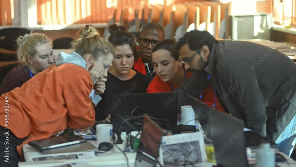 Multiracial group of students are talking and working with laptop at desk at university irrl. Young men and women discussing and looking at computer screen while sitting at table in interior Multiracial group of students are talking and working with laptop at desk at university irrl. Young men and women discussing and looking at computer screen while sitting at table in interior