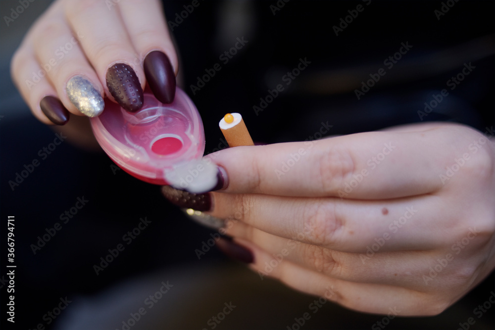 The girl's hands hold capsules for cigarettes and puts them into cigarettes. Banning flavored tobacco. The girl will buy, plozie habits, bypassing the rules.