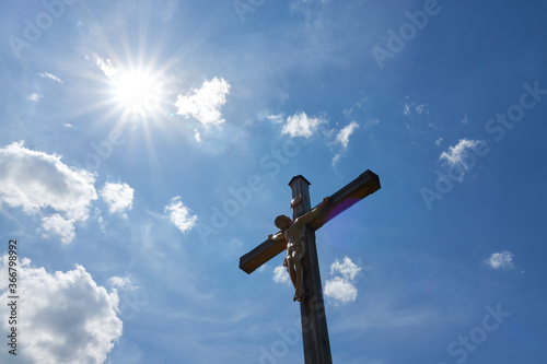 Jesus figure ( cruci fixus ) on brown wooden cross. Blue sky with white clouds. Backlight shot. Germany. photo