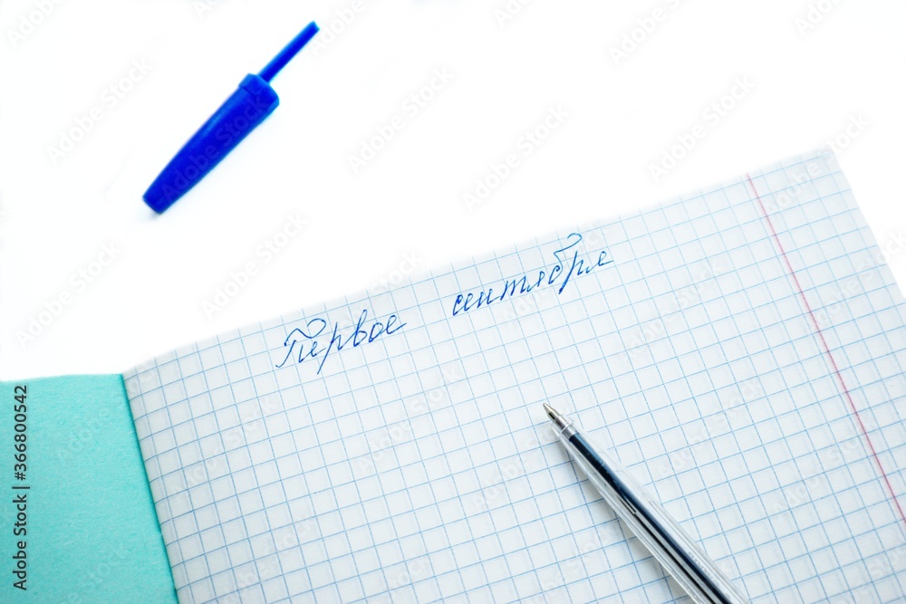 On the first of September, the text in Russian language on a white sheet of notebook in a cage on a white background with a blue ballpoint pen.