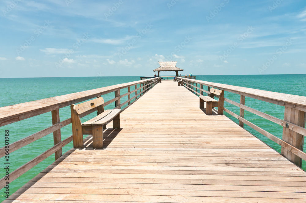 Fototapeta premium front view, of a wood pier with benches, jutting out, one hundred yards, in the tropical waters of the gulf of Mexico, on a sunny morning 