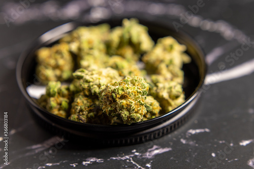 Close up of cannabis buds in black metal container on black marble background