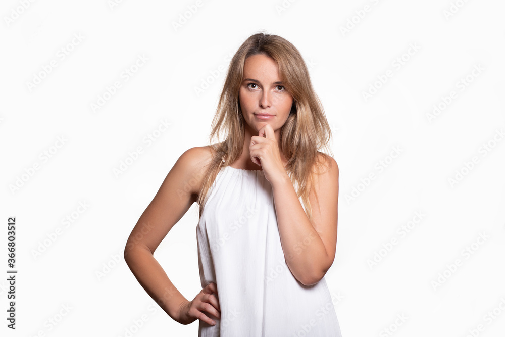 A beautiful showy confident blonde girl with long hair in white dress stands and looks defiantly into the camera on light background. A beautiful showy confident blonde girl with long hair in white dress stands and looks defiantly into the camera on light background.