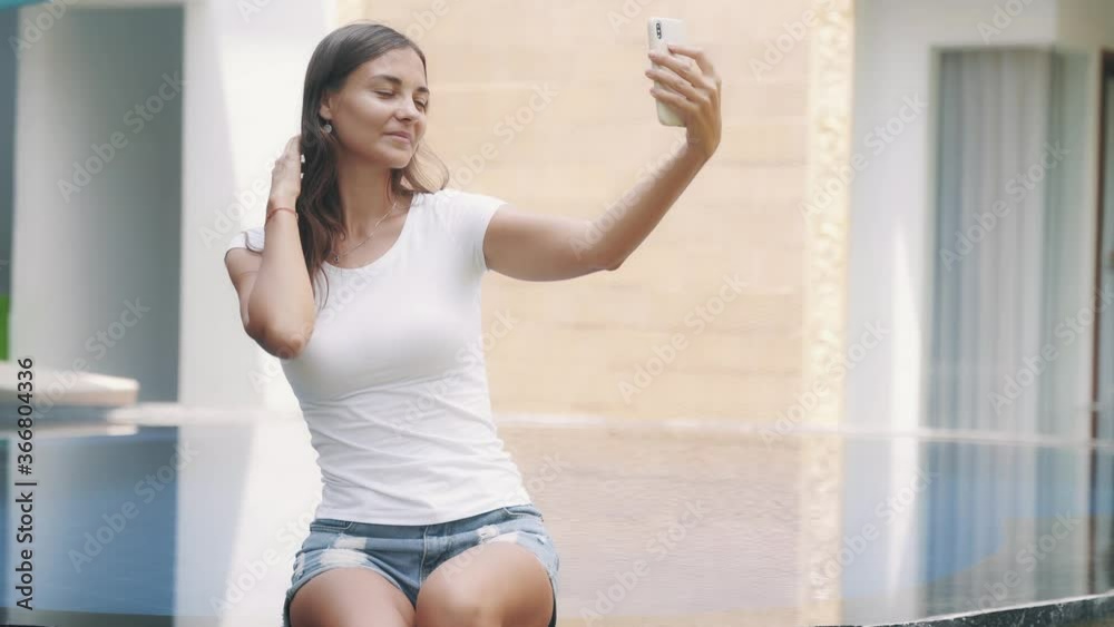 Portrait of beautiful woman makes selfie on phone, sitting on edge of pool Portrait of beautiful woman makes selfie on phone, sitting on edge of pool