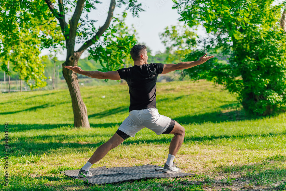 Attractive caucasian young man stretching and doing yoga exercises on the green grass in the park Attractive caucasian young man stretching and doing yoga exercises on the green grass in the park