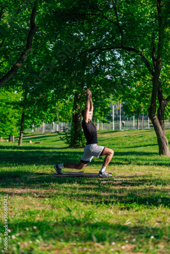 Sporty young man stretching legs and doing forward lunge while having workout at the park © qunica.com