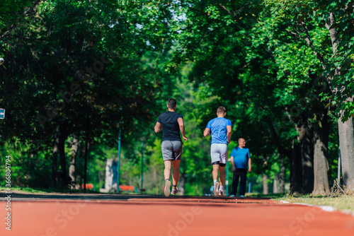 Rearview of two male friends running outdoors in a park