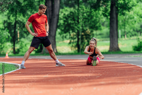 Young couple stretching before starting their morning jogging routine on a tartan track at the park.