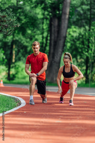Young couple stretching before starting their morning jogging routine on a tartan track at the park.