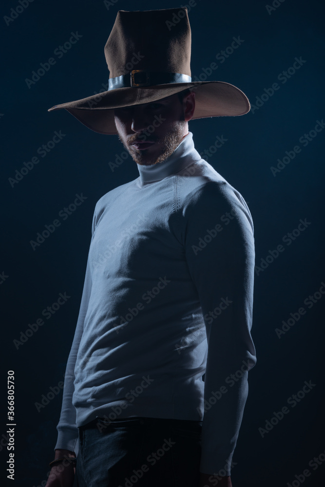 Portrait of a sexy young man with cowboy hat posing in a studio on high contrast and dark background Portrait of a sexy young man with cowboy hat posing in a studio on high contrast and dark background