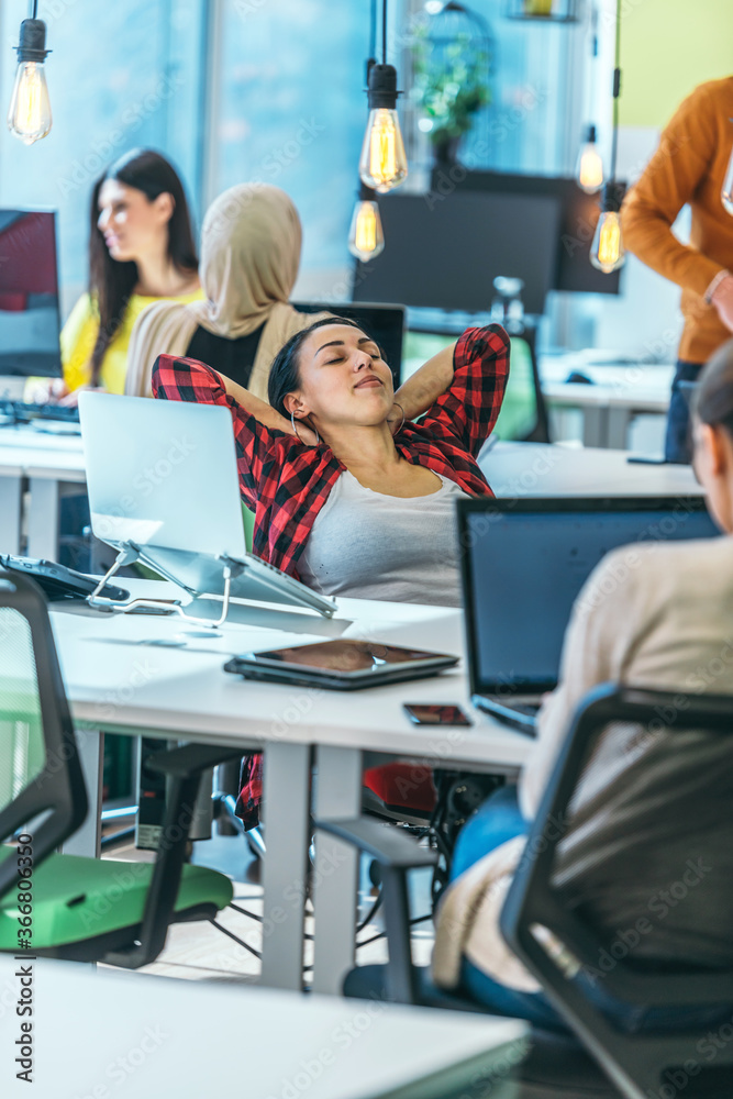 Obraz premium A young worker having a break and resting after solving a task while being surrounded by her colleagues. .