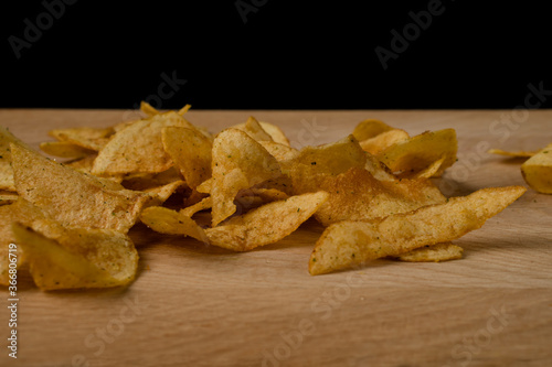 Appetizing potato chips are scattered on a wooden board