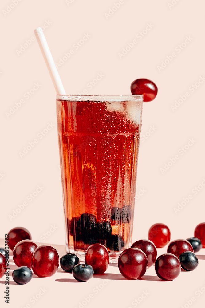 Glass of tasty juice in glass placed on pink background with ripe grapes Glass of tasty juice in glass placed on pink background with ripe grapes