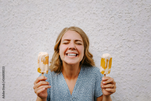 Female with eyes closed making funny grimace faces with tasty ice lollies on sticks on white background photo