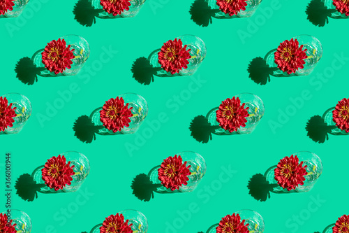 Seamless pattern of a glass with water and deep red flower Dahlia on green background. Minimal flowers concept in hard light with shadows. Art design. Top view, soft focus.