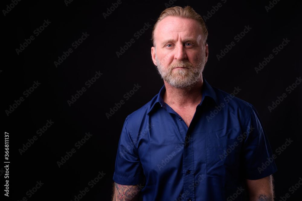 Mature handsome bearded man with blond hair against black background