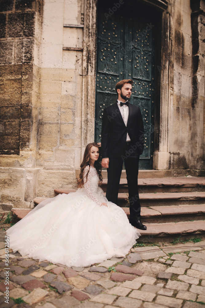 Stylish bride and groom gently hugging on european city street. Gorgeous wedding couple of newlyweds embracing near ancient building. romantic sensual moment of newlyweds Stylish bride and groom gently hugging on european city street. Gorgeous wedding couple of newlyweds embracing near ancient building. romantic sensual moment of newlyweds
