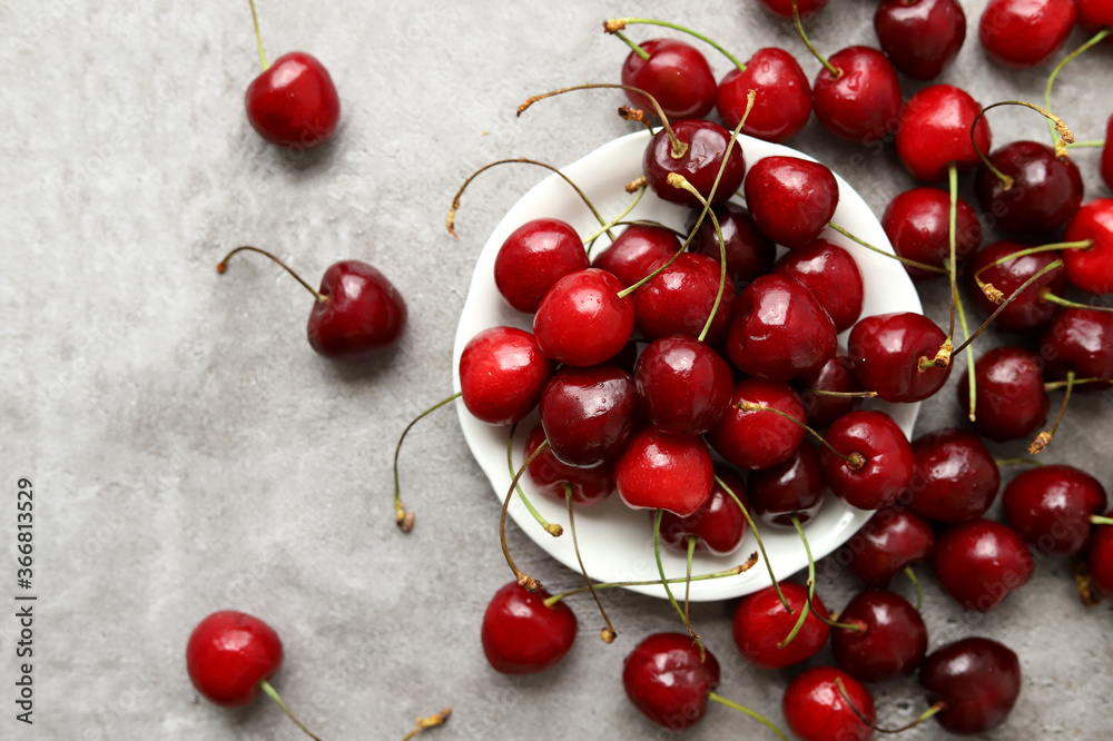 Scattered fresh cherries on a small white plate on a gray cement surface. Selective focus. The harvest of berries. Delicious natural healthy dessert. Scattered fresh cherries on a small white plate on a gray cement surface. Selective focus. The harvest of berries. Delicious natural healthy dessert.