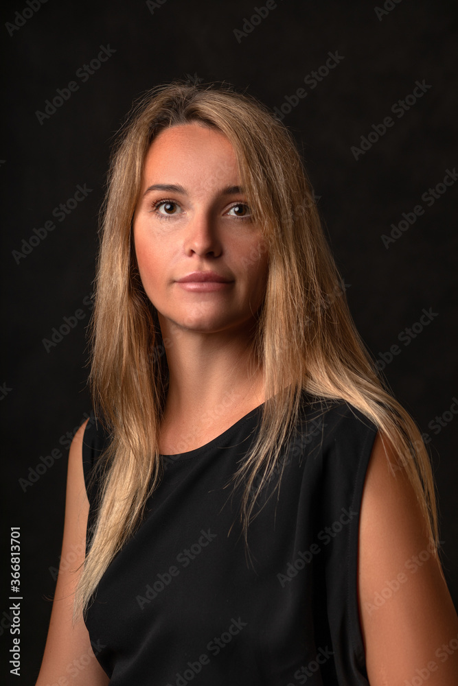 Peaceful calm beautiful girl in a black dress on a dark background, portrait of a 30 year old woman with long blonde hair.